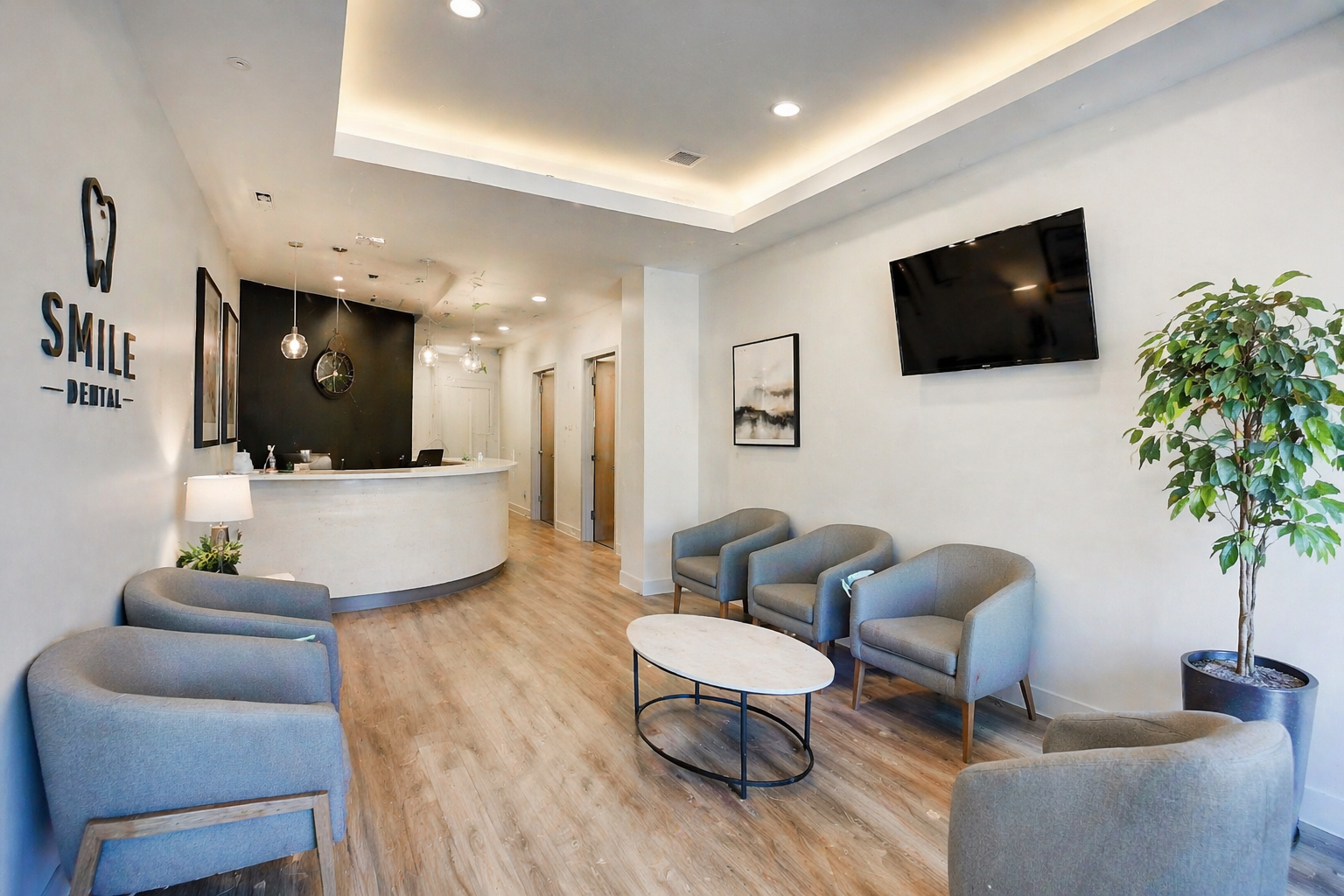 Clean modern dental office waiting room with comfortable gray chairs, a potted plant, and warm recessed lighting
